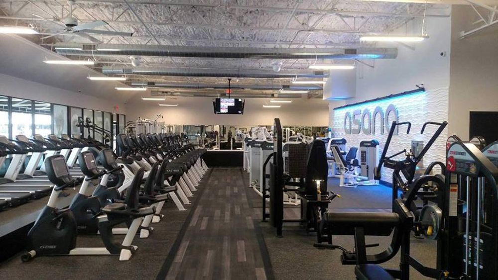 A modern gym interior with rows of exercise equipment and bright overhead lights.