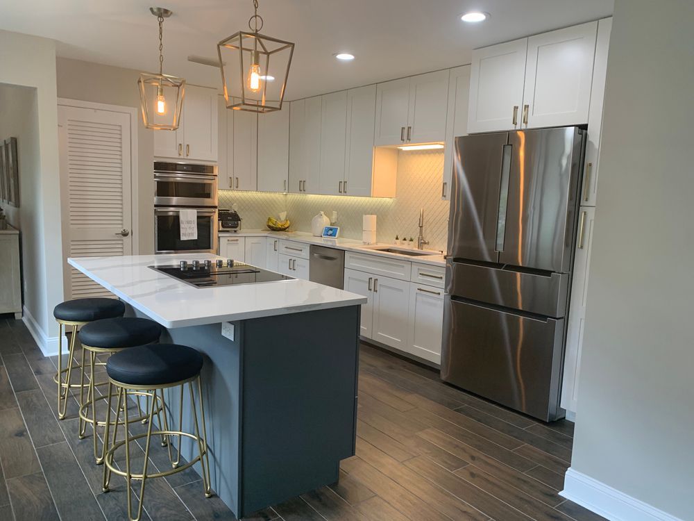 Modern kitchen: white cabinets, stainless steel fridge, island with cooktop, gold stools, dark floor.
