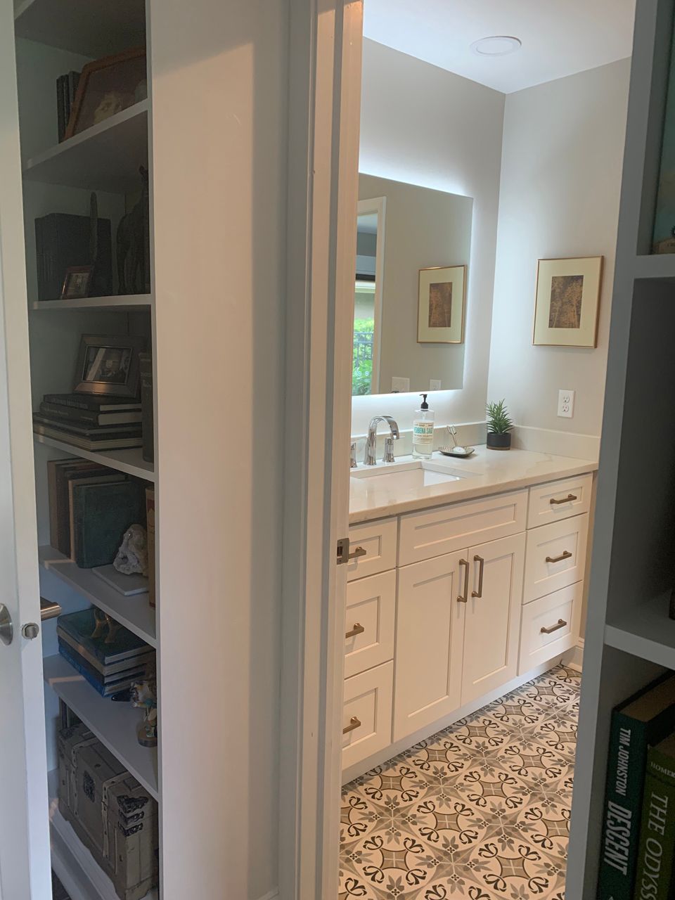Bathroom with white cabinets, gray patterned floor, and a bookshelf visible on the left.
