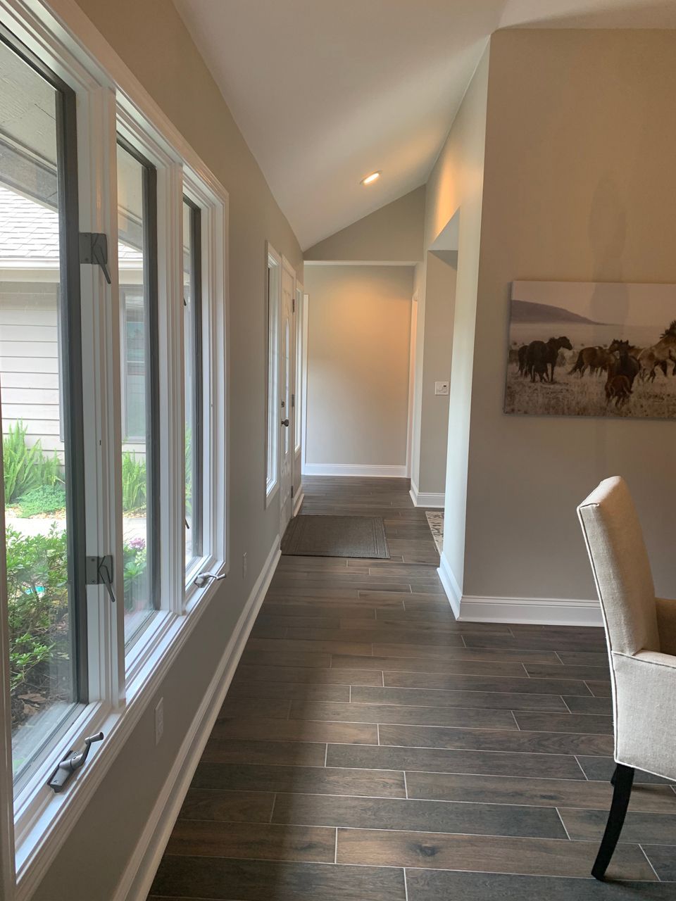 Long, dark wood-floored hallway with windows and a painting of horses.