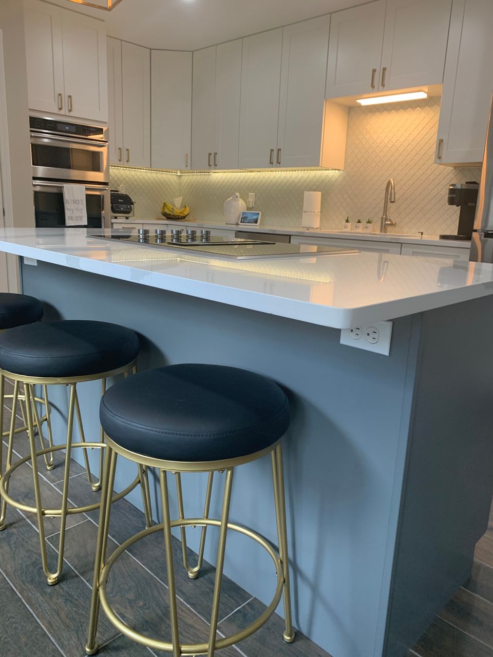 Modern kitchen with island bar stools. White and gray cabinets, marble counters, gold stools.