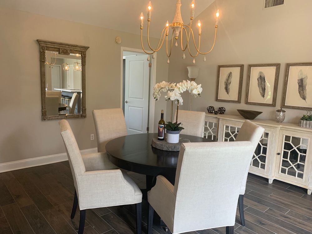 Dining room with a round table, chairs, mirror, chandelier, and buffet with framed feathers.