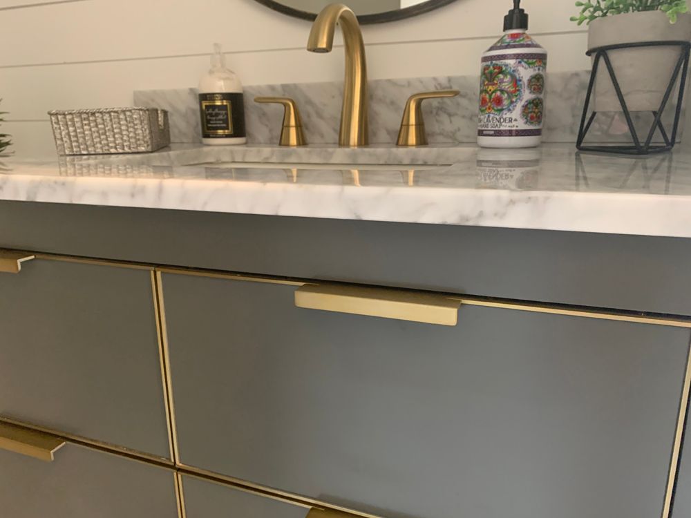 Gray bathroom vanity with gold hardware, marble countertop, and gold faucet.