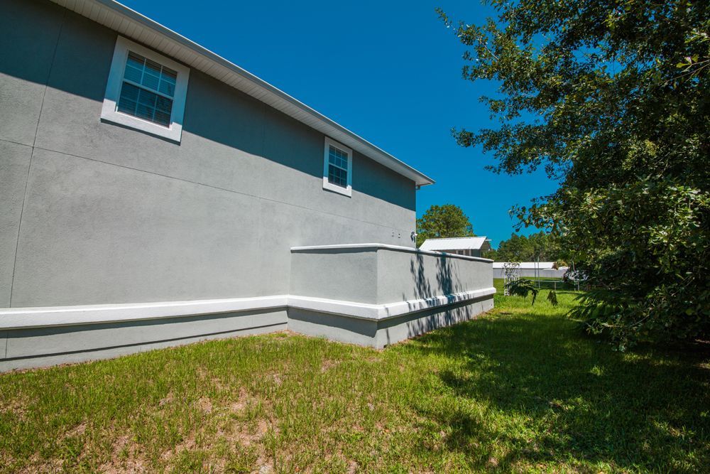 Gray house exterior with grass and trees under a blue sky.
