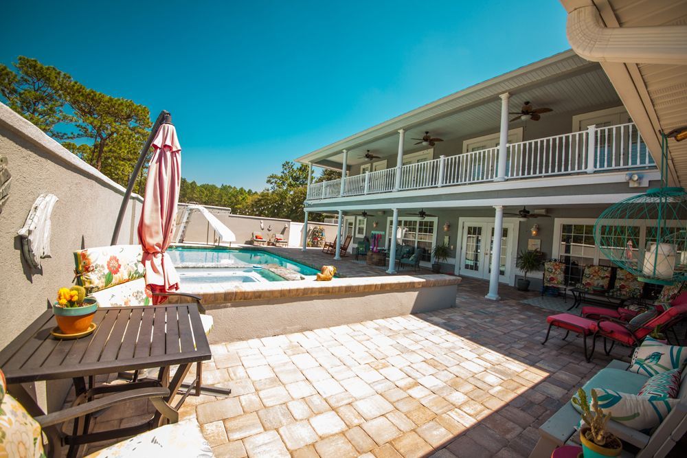 Backyard patio with pool, seating areas, and a two-story house with a blue sky.
