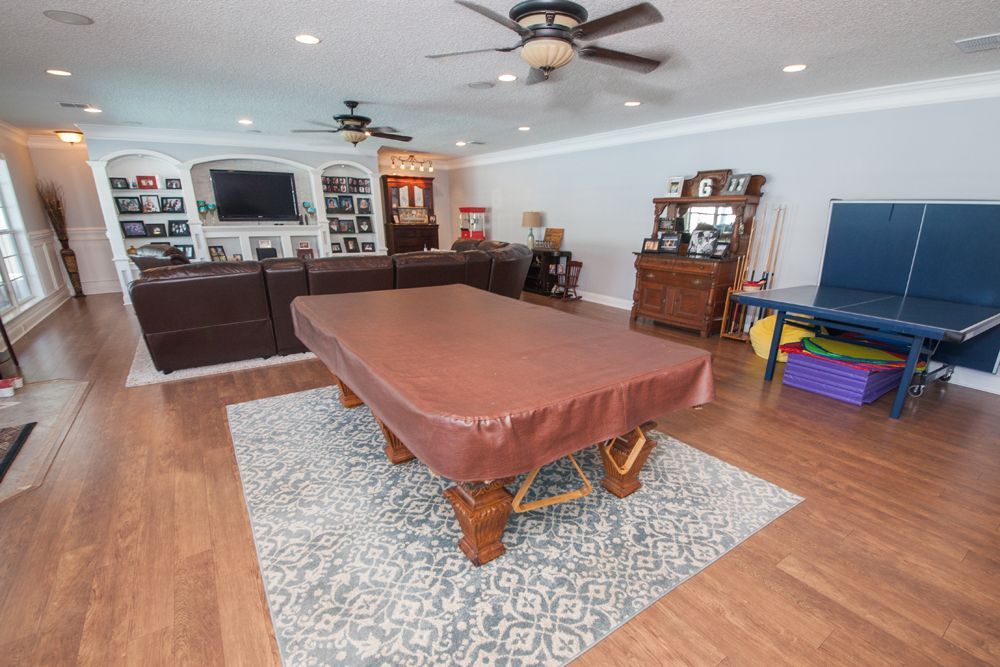 A living room with a pool table covered by a brown cloth, brown leather sectional, and other furniture.