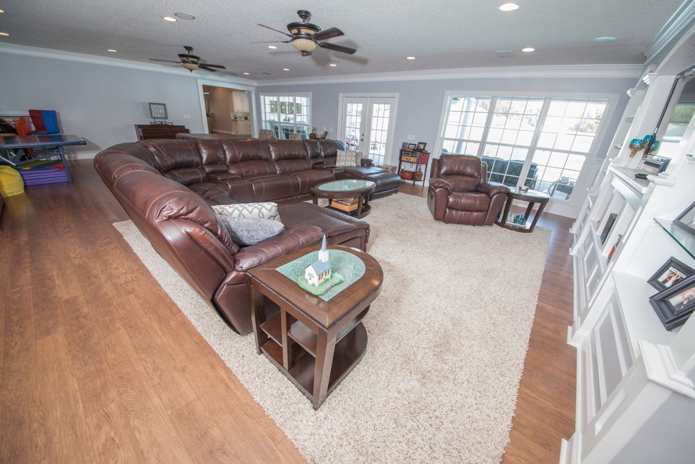 Spacious living room with brown sectional, recliner, and a light rug, hardwood floor, and large windows.