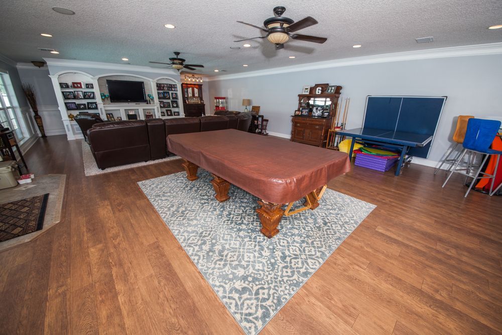 Spacious living room with a pool table, seating area, and built-in entertainment center on hardwood floors.
