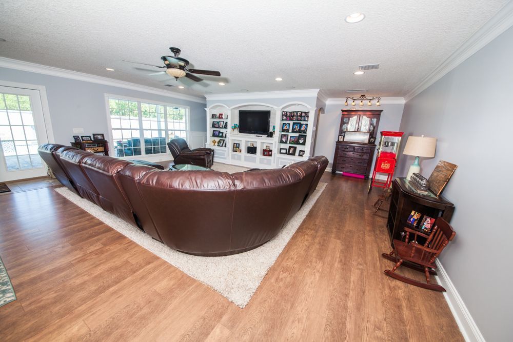Spacious living room with brown leather sectional, wooden floors, and built-in entertainment center.