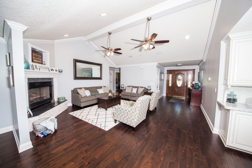 Spacious living room with fireplace, sofas, patterned rug, dark wood floor, and entry door.
