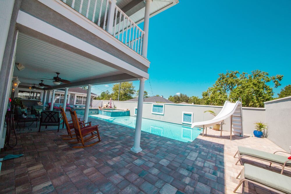 Patio with a pool, water slide, and second-story balcony, blue sky overhead.