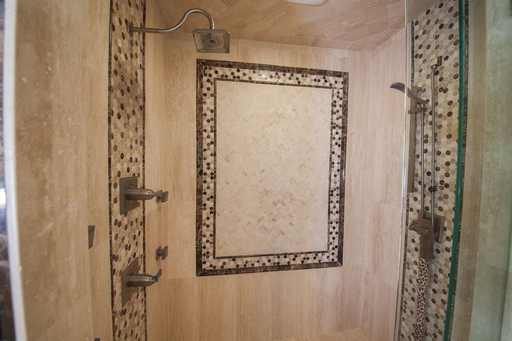 Shower with beige tile walls, mosaic tile border, glass door, and showerhead.