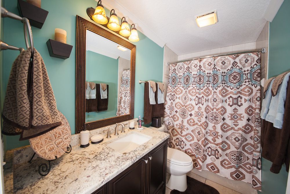 Bathroom with teal walls, brown vanity, and patterned shower curtain.