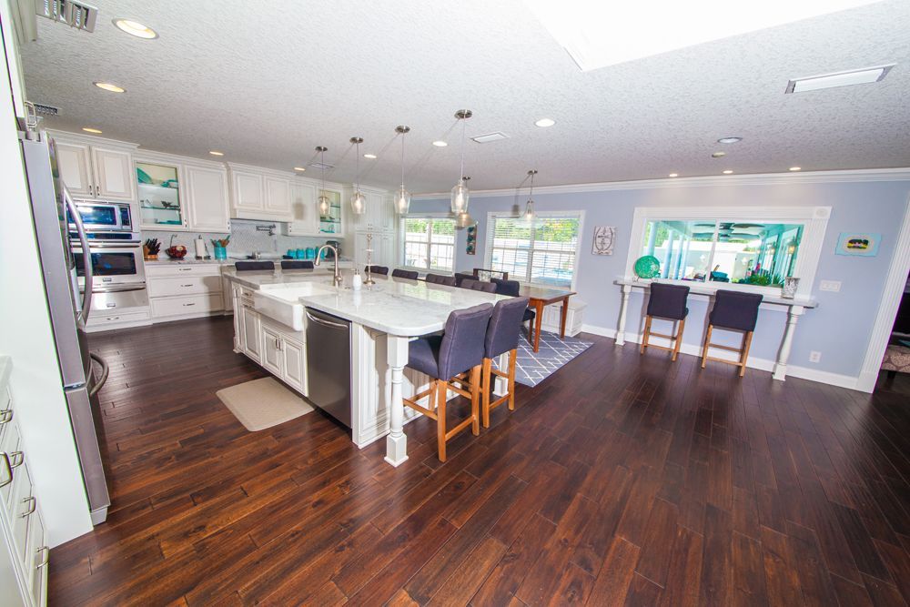 Spacious kitchen with white cabinets, large island, dark wood floors, and blue accents.