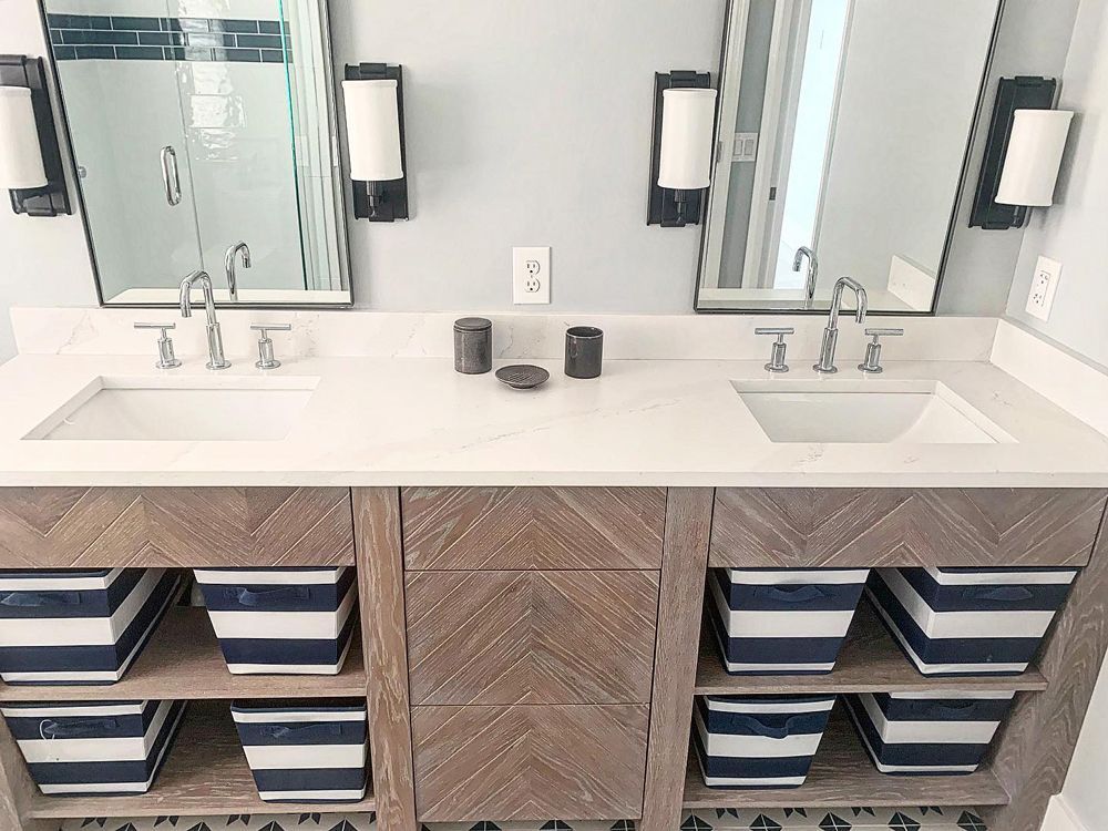 Bathroom with double vanity, light gray walls, two mirrors, and blue striped storage bins.