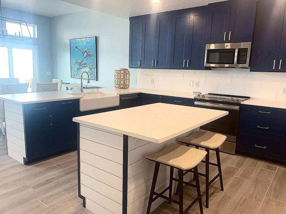 Blue and white coastal kitchen with island seating, stainless steel appliances, and light wood floors.