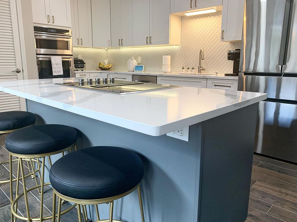 Modern kitchen with white countertop island, blue stools, stainless steel appliances, and gray cabinets.