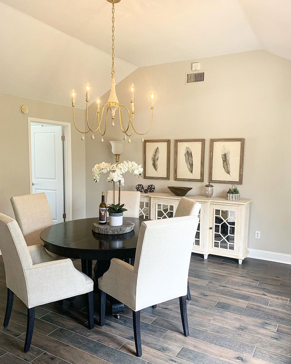 Dining room with round black table, cream chairs, white buffet, and a gold chandelier.