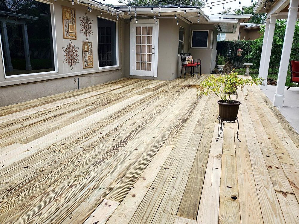 Wooden deck on a house's back exterior with windows, a door, and a potted plant. String lights overhead.