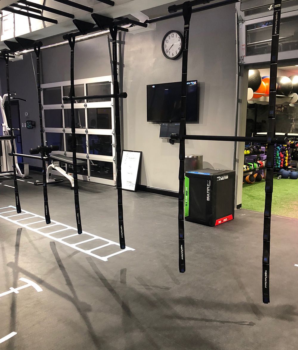 Gym interior with pull-up bars, a clock, TV, and box, with floor markings, and a garage door.