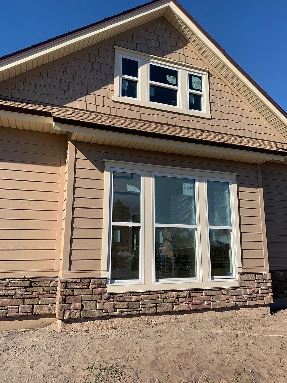Tan house exterior with stone base, multiple windows, and a gable roof.