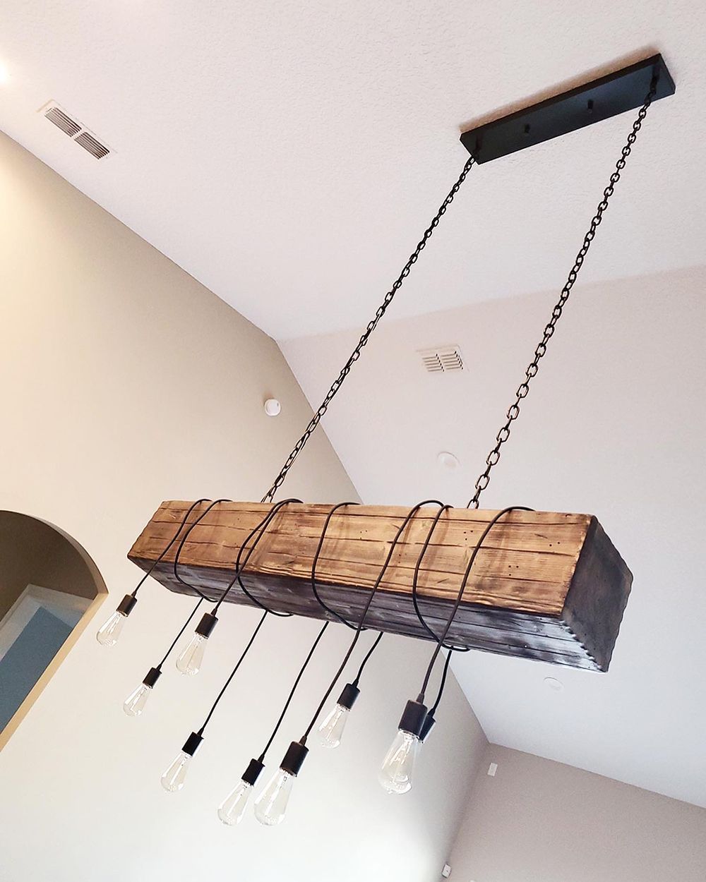 Rustic wooden beam chandelier with exposed bulbs hanging from a high ceiling.
