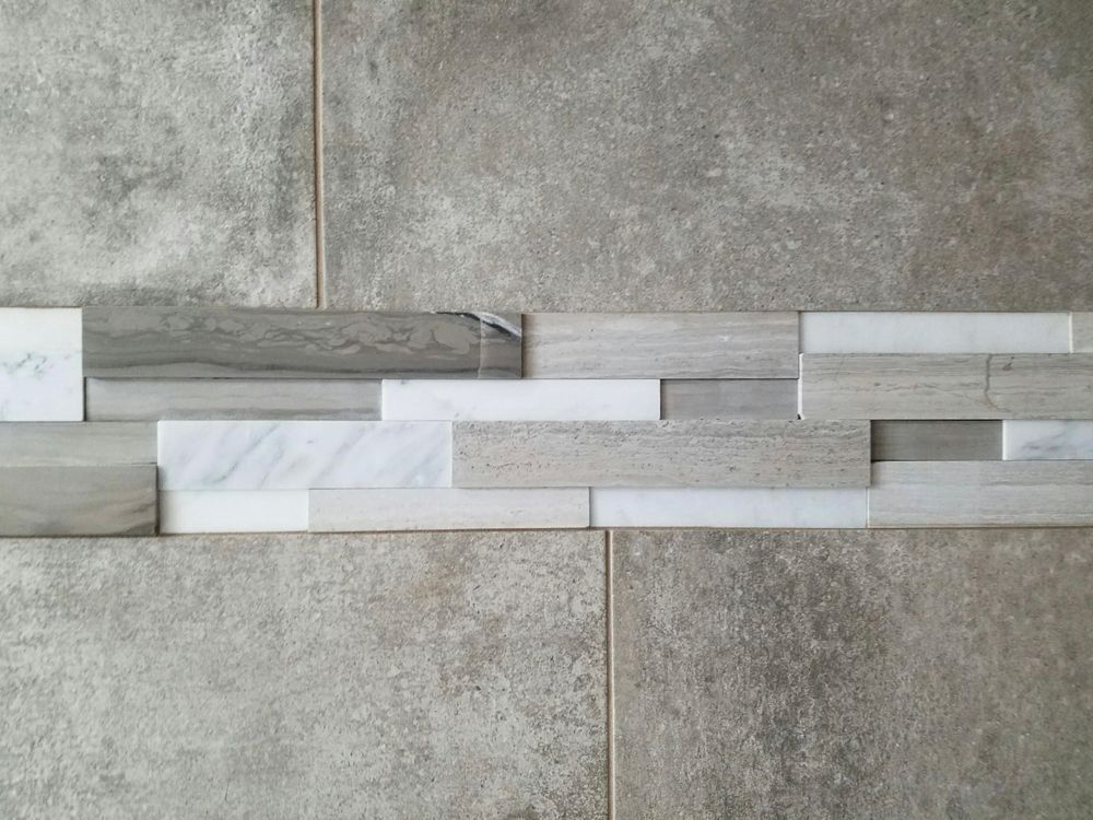 Gray and white tile wall with a horizontal strip of varied rectangular tiles.