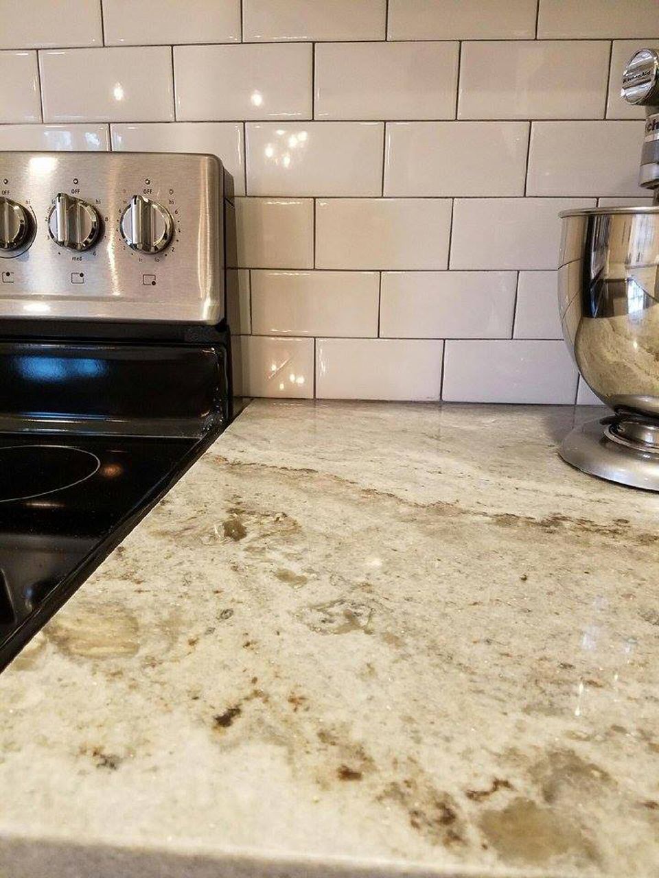 Countertop with granite surface, stove, and mixer in a kitchen. Subway tile backsplash.