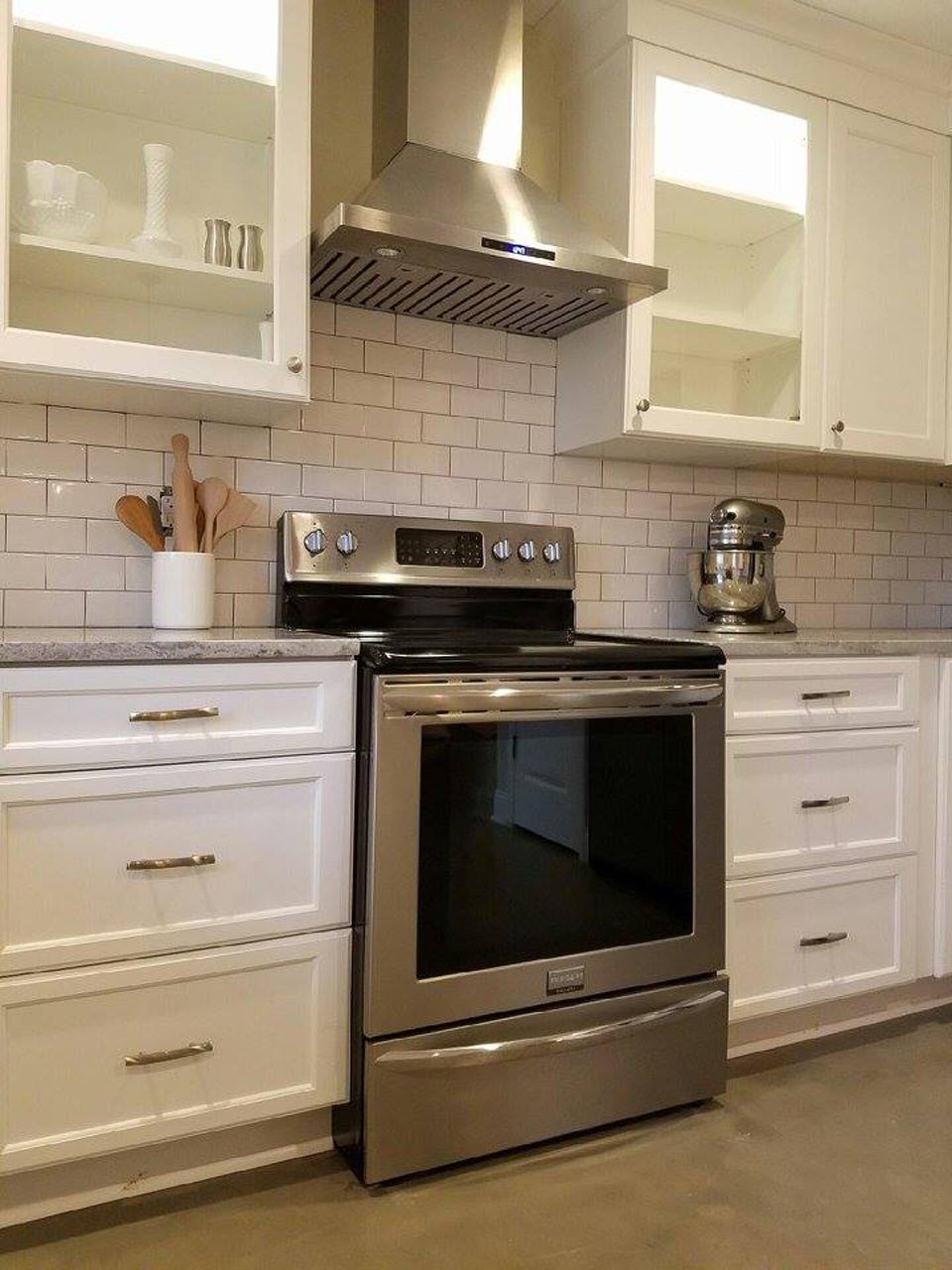 Stainless steel oven centered in a white kitchen with cabinets, range hood, and subway tile backsplash.