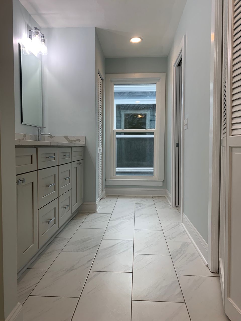 Bathroom with light blue walls, white vanity, window, and tiled floor.