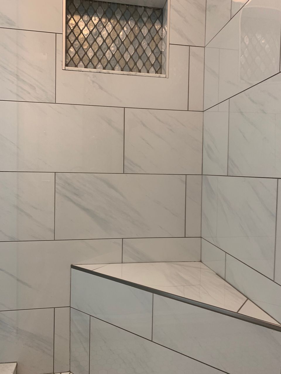 White tiled shower with built-in corner seat and decorative niche, gray grout lines.