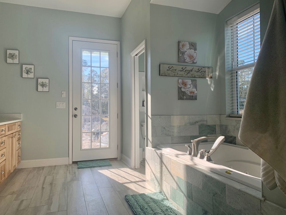 Bathroom with tub, door to outside, and artwork on the wall. Soft green walls, natural light.