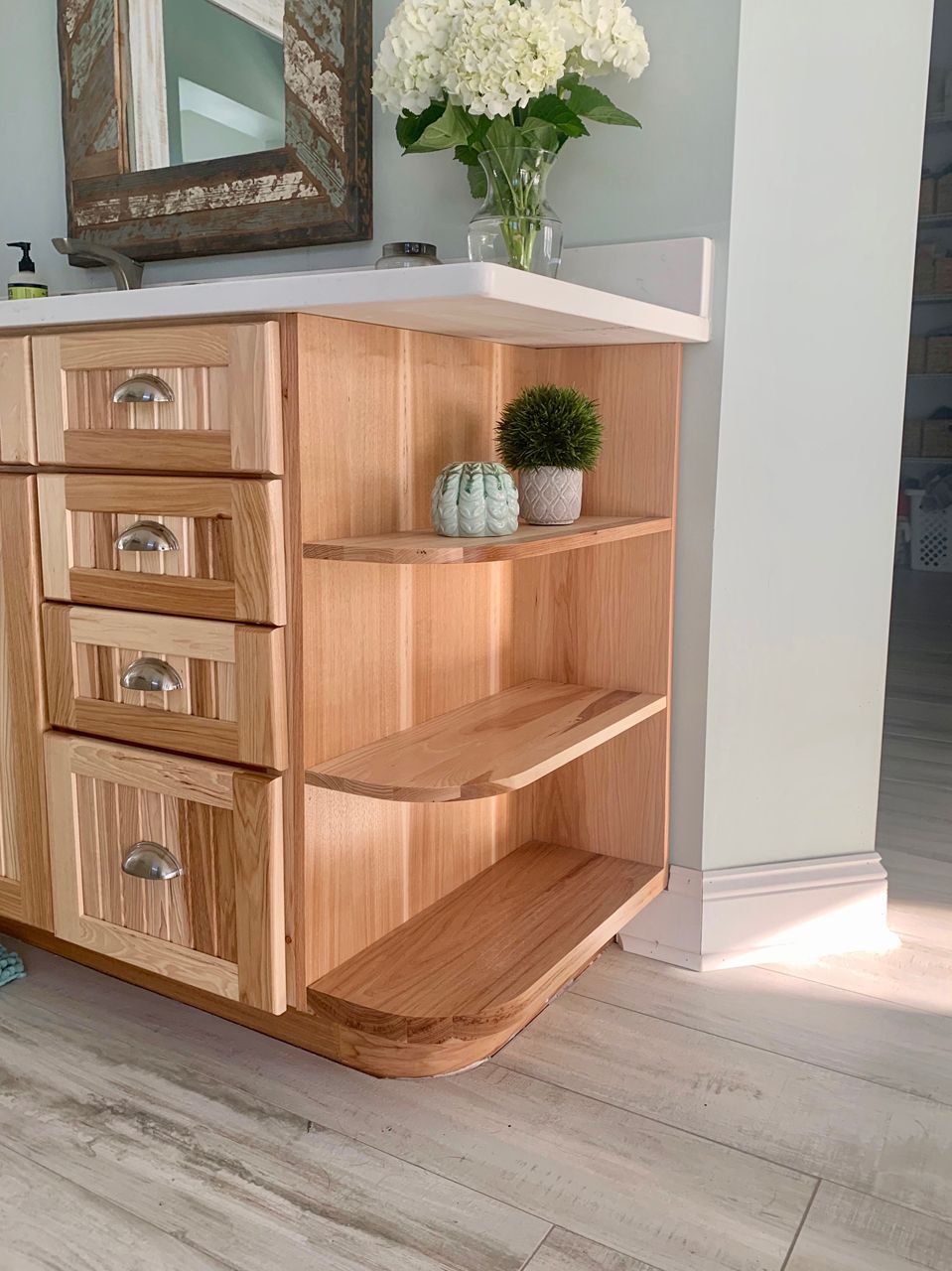 Light wood bathroom vanity with open shelving and decorative items.