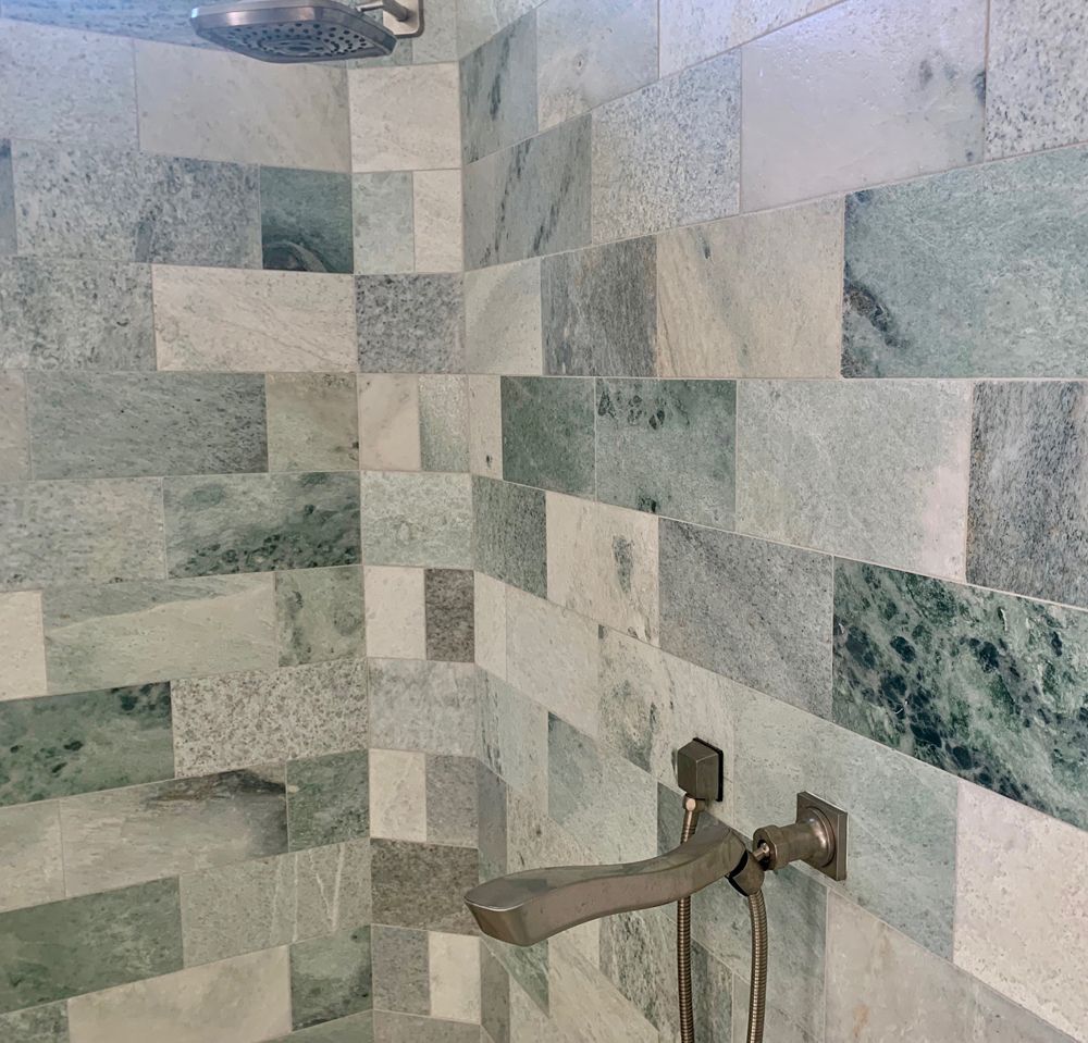 Shower with green and white marble tile walls and silver fixtures.