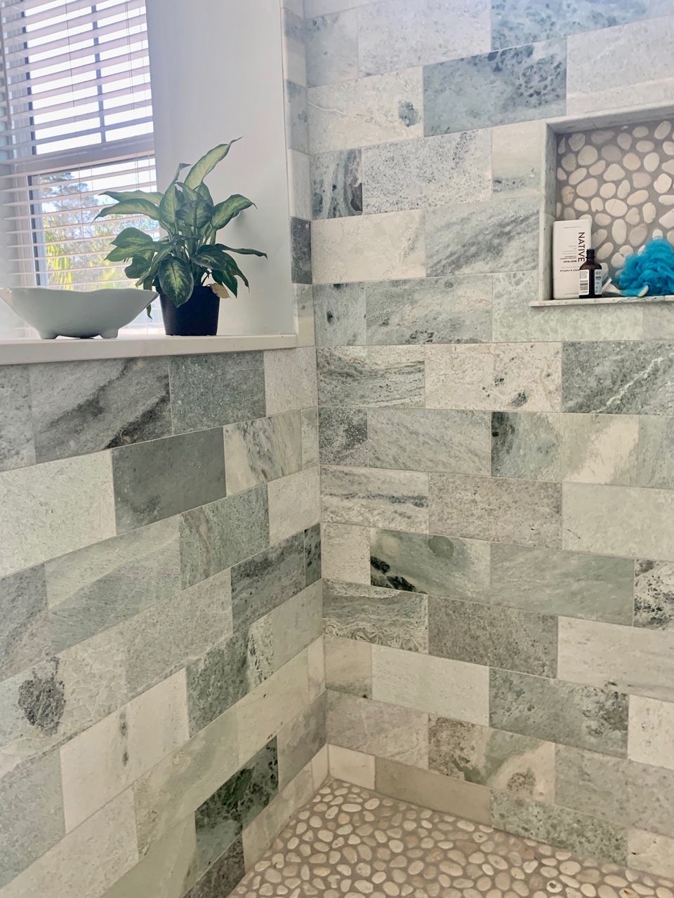 Bathroom with light green, blue, and white marble tile. A plant sits by the window.