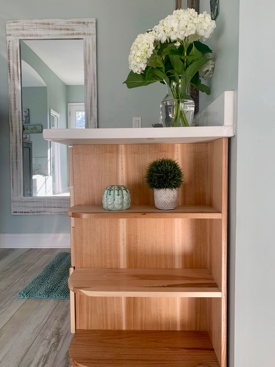 Wooden bookshelf with decorative items: flowers, plants, and shells, against a pale blue wall.