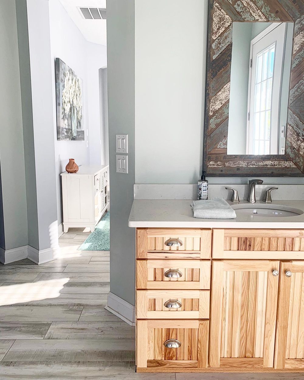 Bathroom with wooden vanity, mirror, and doorway leading to another room.