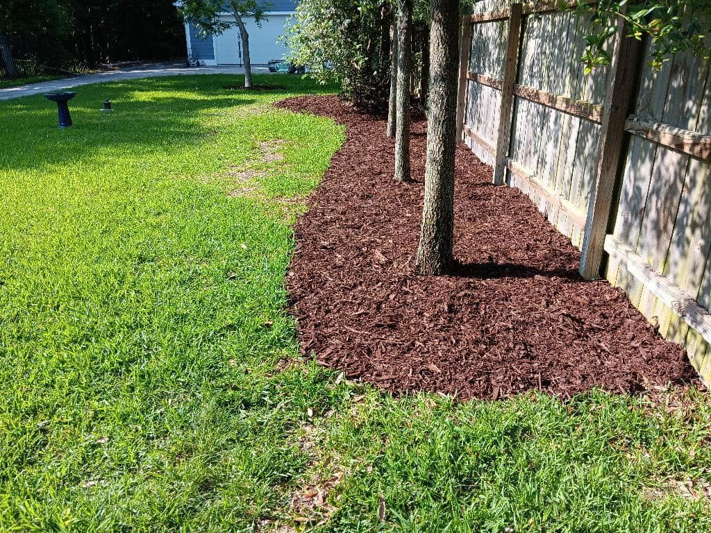 A fence is surrounded by a lush green lawn and mulch.