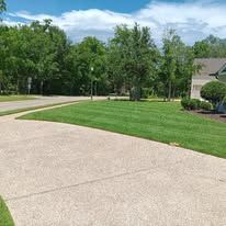 A concrete driveway leading to a house with a lush green lawn.