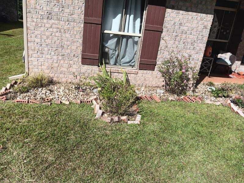 A brick house with brown shutters and a lush green lawn in front of it.