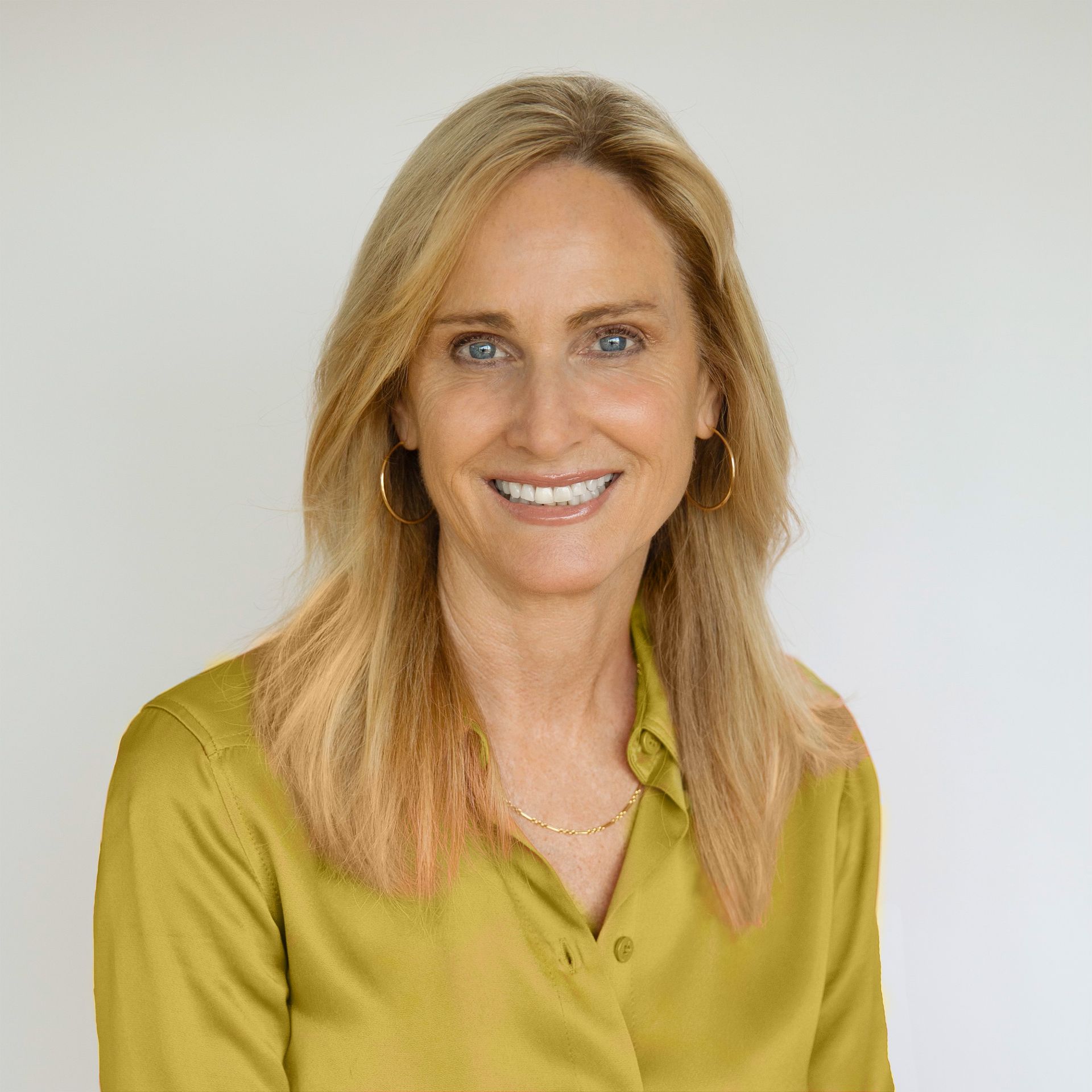 Smiling blonde woman in a green blouse against a light gray background