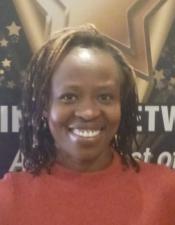 Naomi Mia Williams Person smiling, wearing an orange shirt, with braided hair, in front of a blurred background with text and stars.