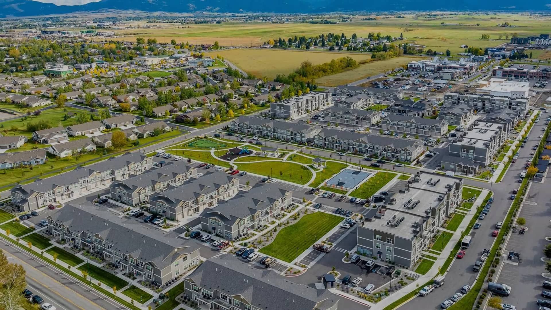 Aerial view of a large residential area with gray buildings, green spaces, and a road.