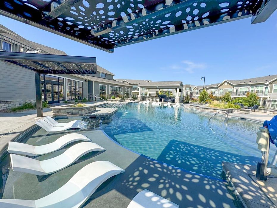Poolside scene with white lounge chairs, shaded pergola, and clear blue water.