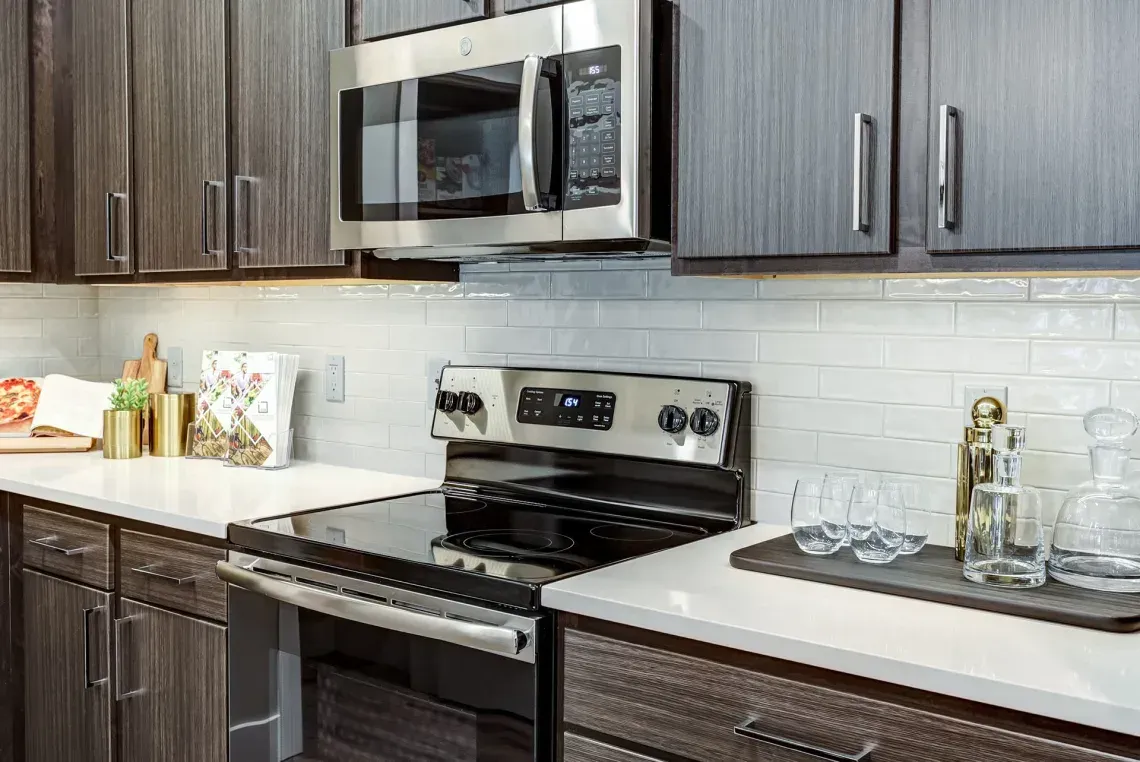 Modern kitchen with stainless steel microwave and oven, dark cabinets, white countertops, and white tile backsplash.