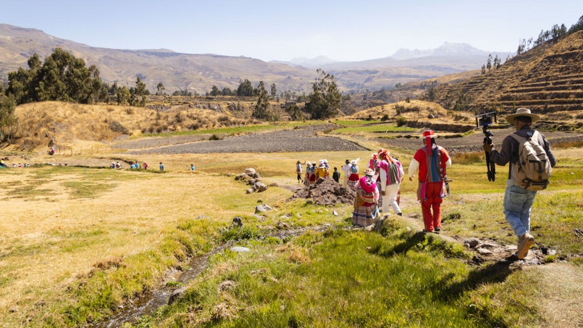 Senderistas caminan por un sendero cubierto de hierba a través de un valle de montaña iluminado por el sol