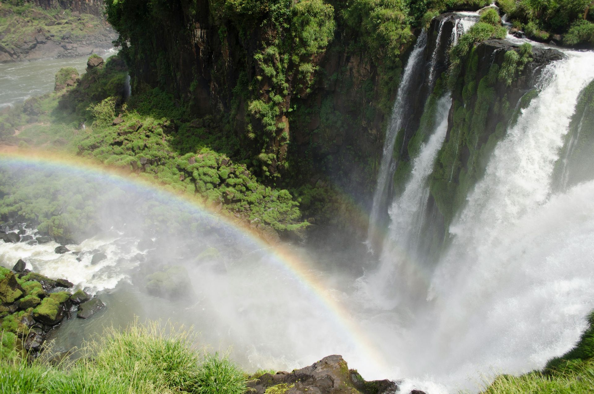 Cascada que se precipita en un desfiladero exuberante con niebla y un arcoíris que se extiende sobre el rocío.