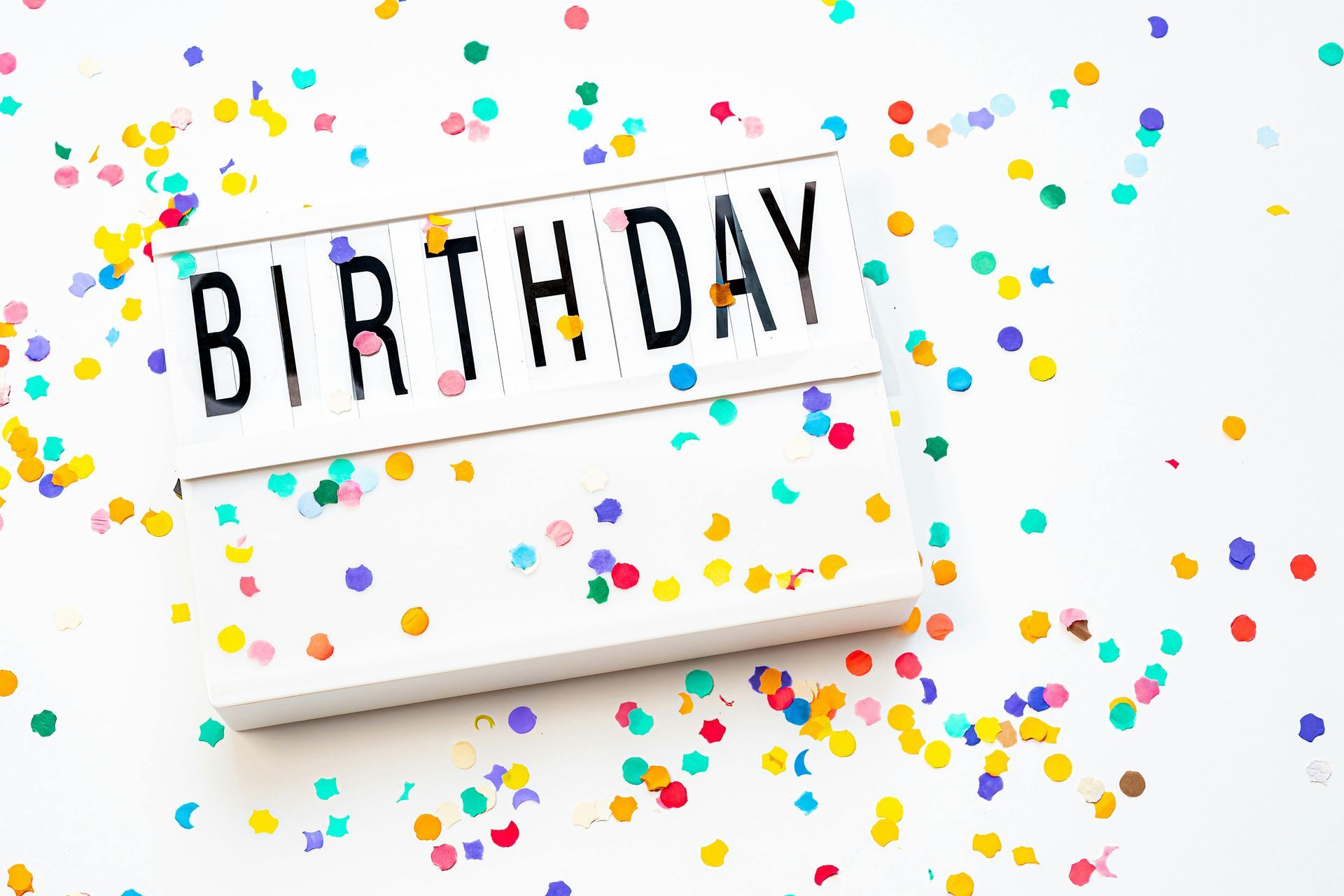 A birthday sign surrounded by colorful confetti on a white surface.