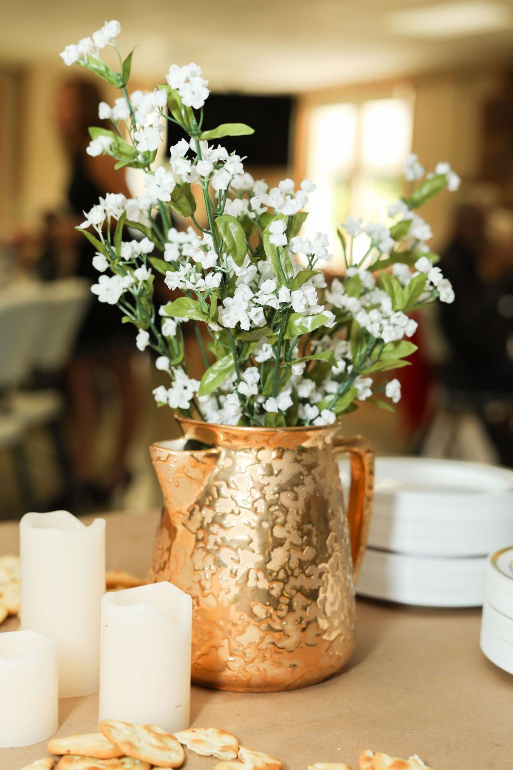 A copper pitcher filled with white flowers sits on a table.