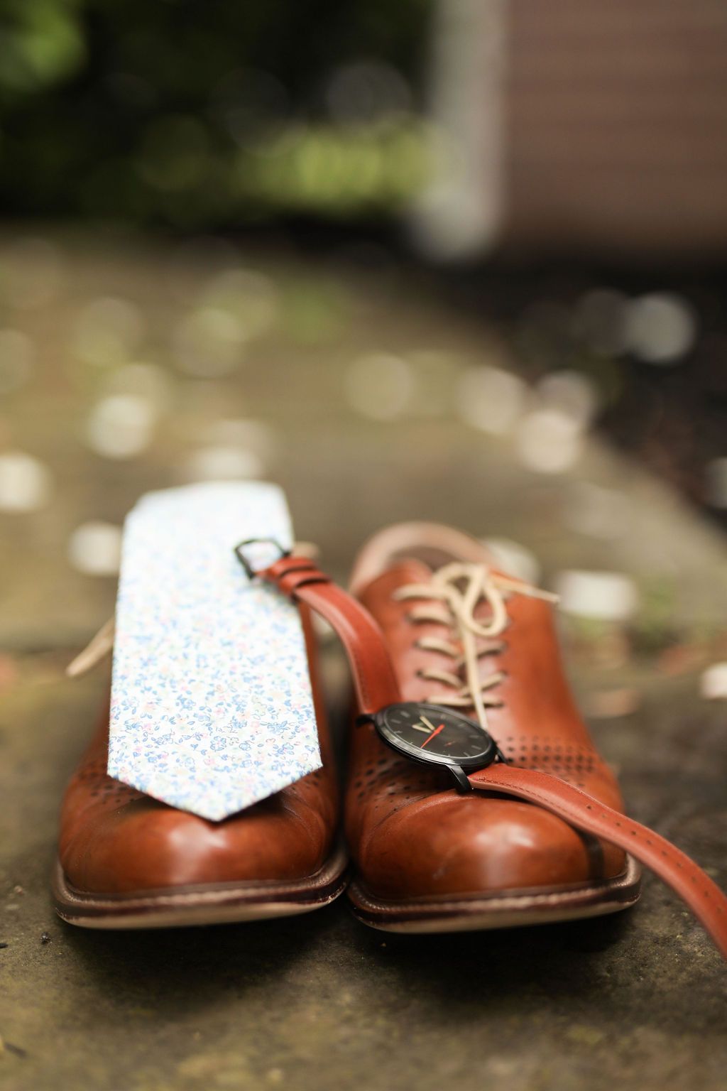 A pair of brown shoes with a tie and watch attached to them.